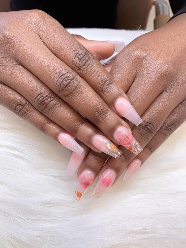 A woman's beautiful hands with long coffin acrylic nails that fade from clear to pale pink that has flowers nail designs on select nails
