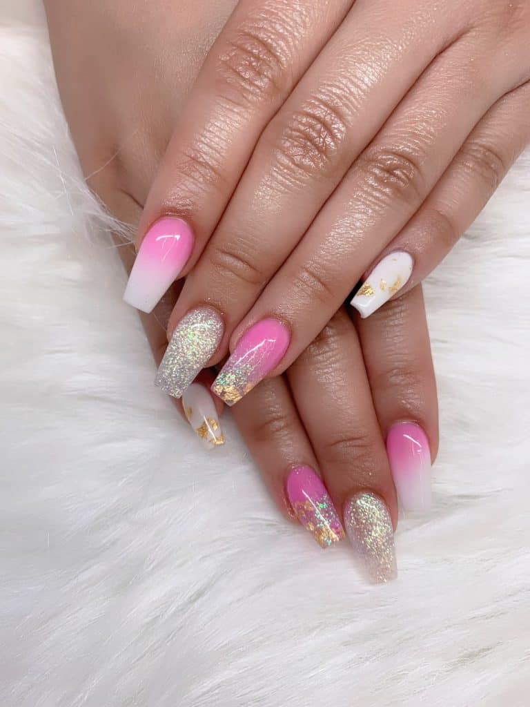 A woman's hands with beautiful pink-and-white ombre nails that has dash of glitter and patterns of gold foil nail designs on select nails