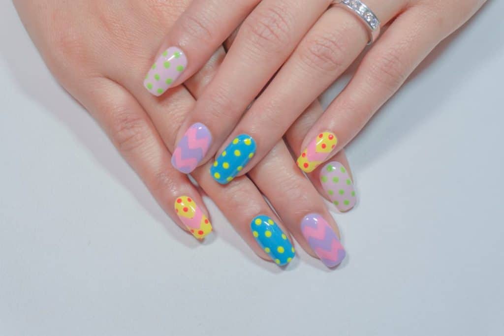 A woman's hands with multicolored acrylic nails that has polkas and zigzags in striking colors nail designs
