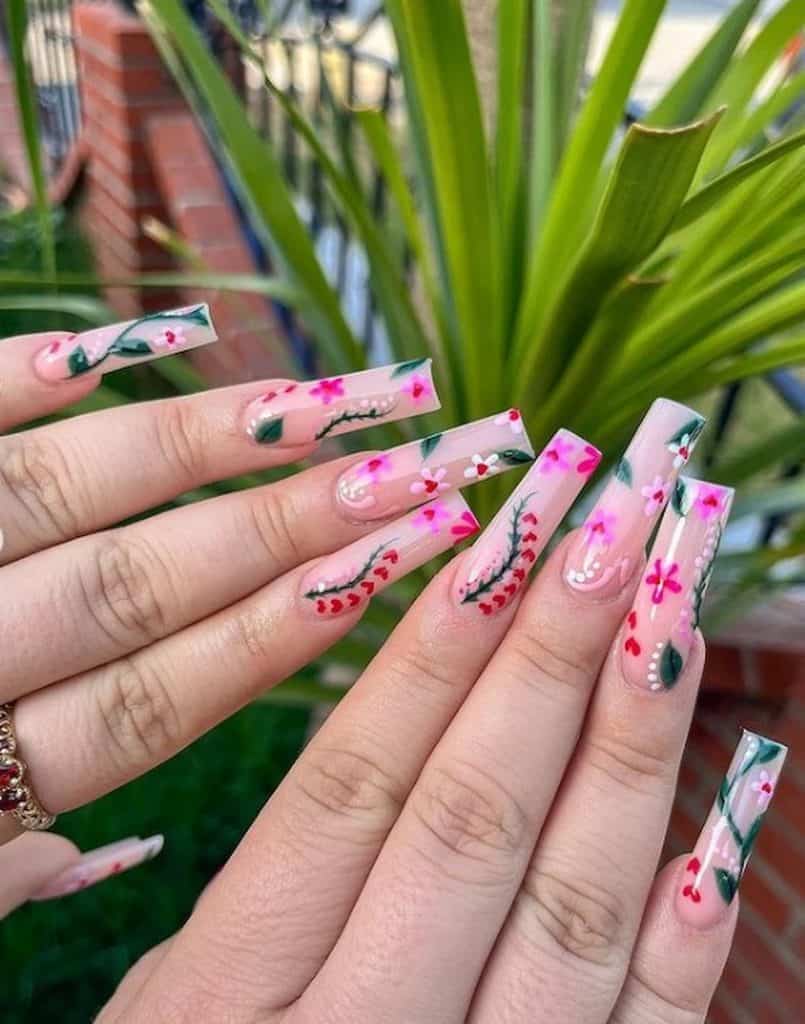 A closeup of a woman's hands with a sheer pink nail polish base that has flowers, vines, leaves, hearts, and dots nail designs