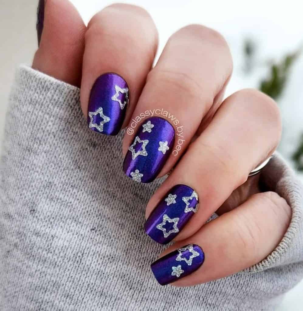 A woman's beautiful hand with a blue nail polish base that has silver stars nail designs