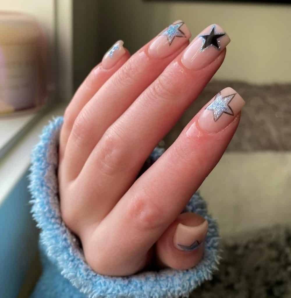 A woman's hand with a beautiful nude nail polish that has medium sized stars outlined in black with black and blue glitters nal designs