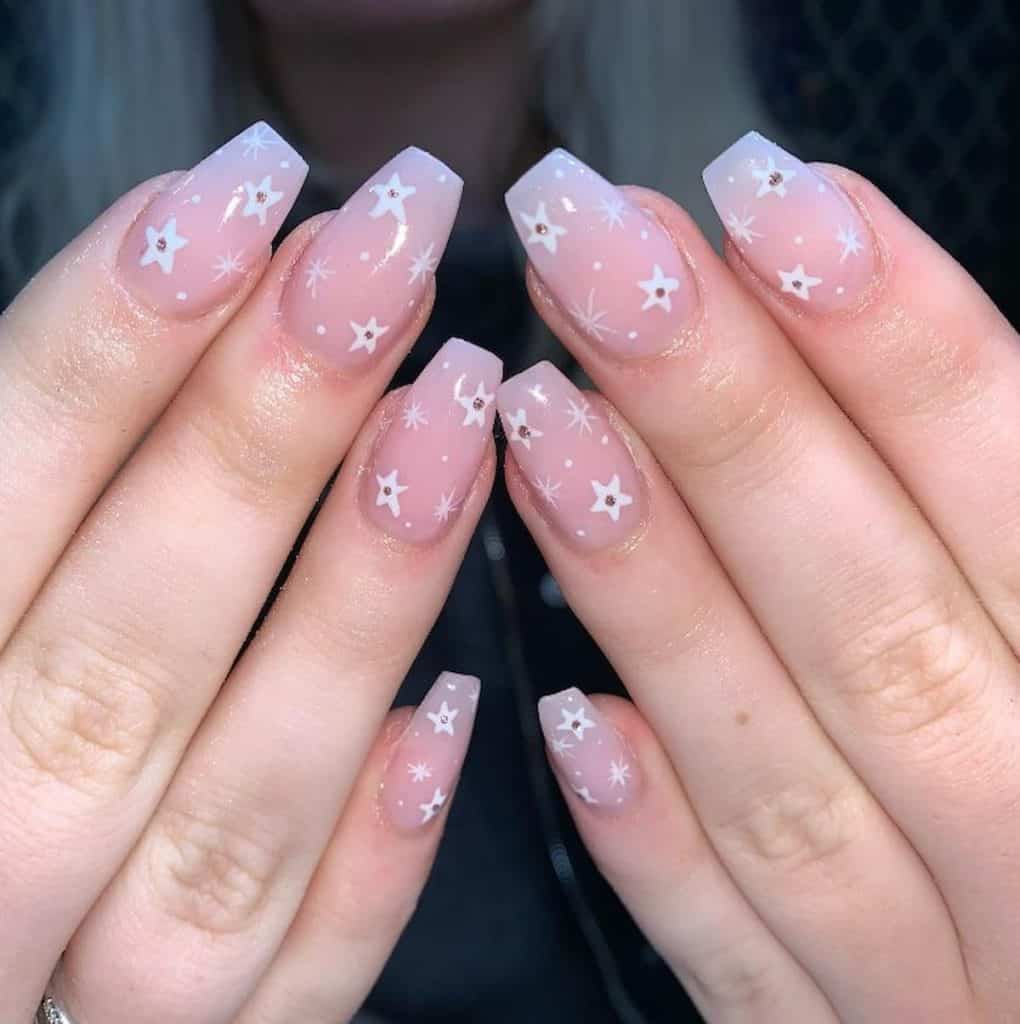 A closeup of a woman's hands with pinkish nude nail polish base that has white twinkling stars and pink gems nail designs
