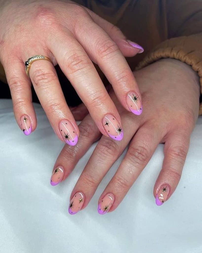 A closeup of a woman's hands with nude nail polish base that has black stars and dots nail designs