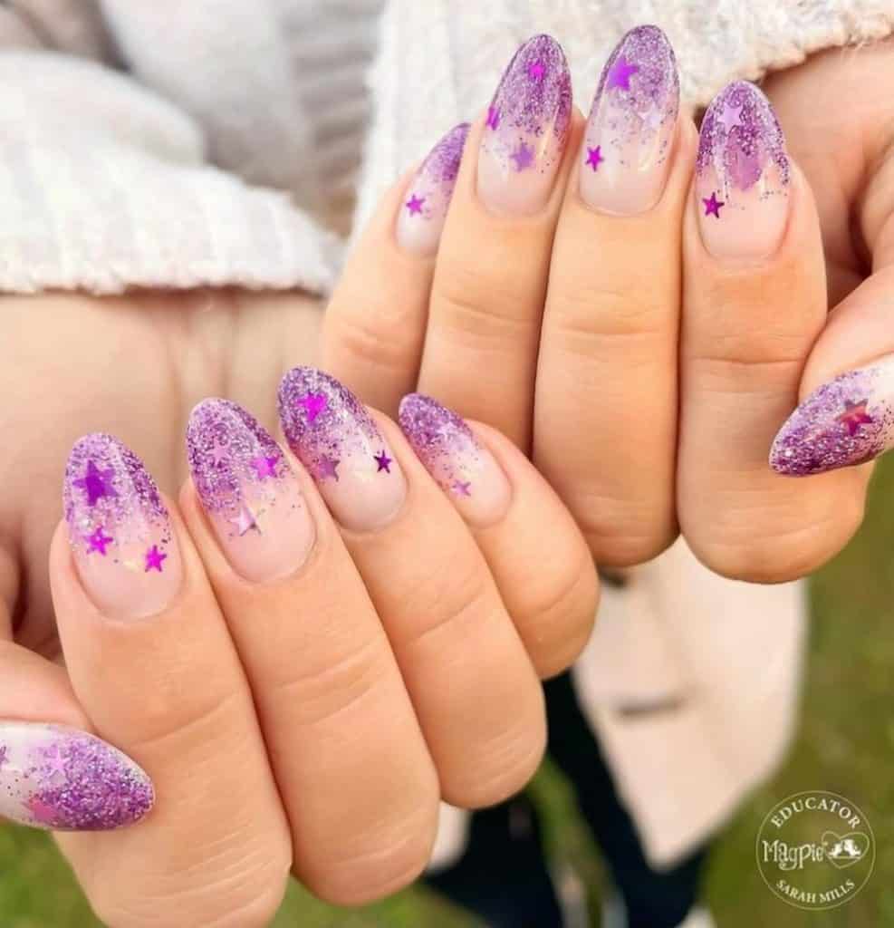 A closeup of a woman's hands with half-nude and half-purple glitter ombré nail polish that has purple chrome stars nail designs