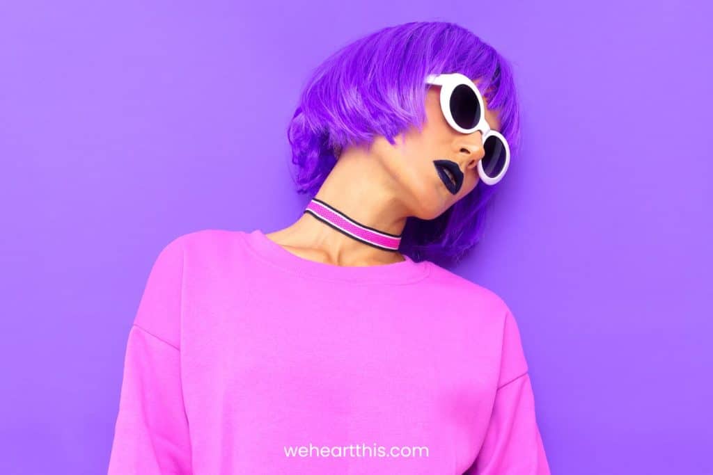 Stylish girl with purple hair wearing sunglasses and purple sweater on a purple background