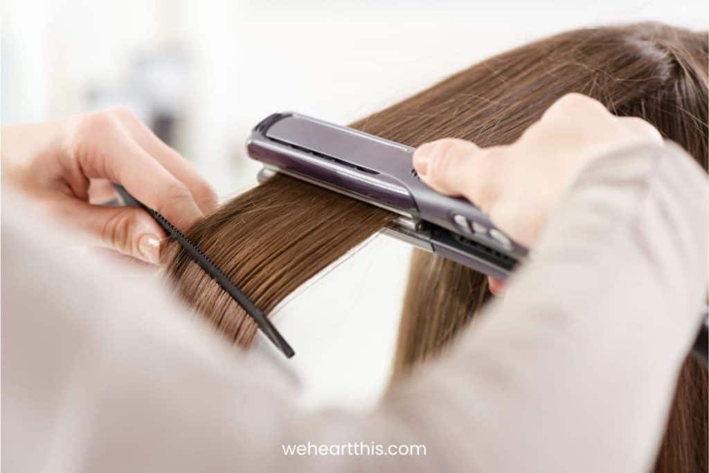 hairdresser straightening long brown hair using hair straightener in a salon