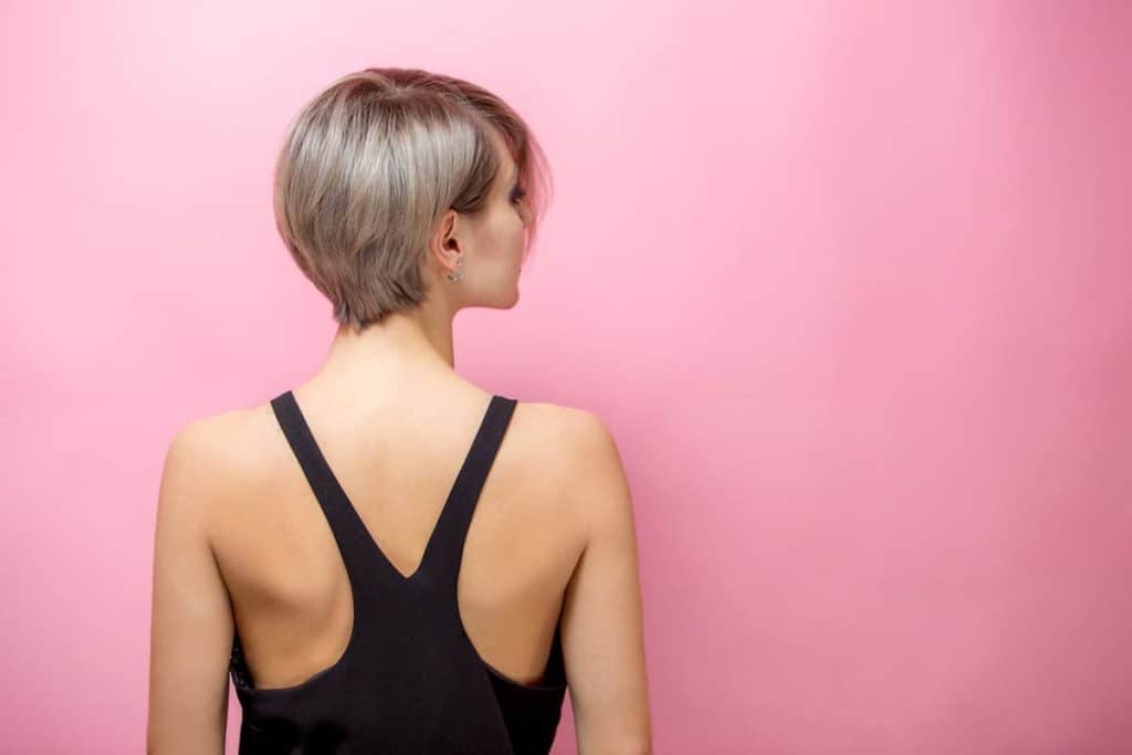 The back of a woman with short ash blonde haircut isolated on a pink background