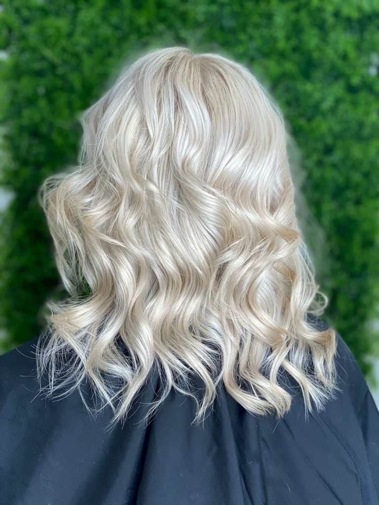The back of a medium-length, platinum blonde and curly haired woman with brown lowlights