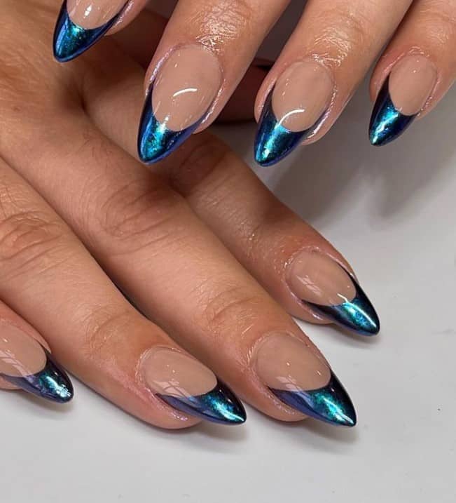 A closeup of a woman's hands with a glossy nude nail polish base that has blue chrome nail tips 
