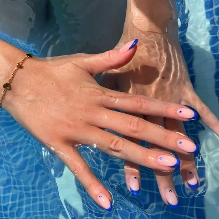 A woman's hands with peach nail polish base that has matte blue French tips and tiny eyes nail art