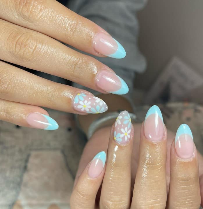 A closeup of a woman's hands with pale pink nail polish base that has baby blue French-tip nails with white and baby blue daisies