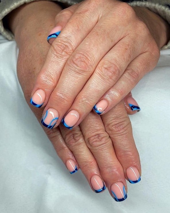 A woman's hands with a glossy nude peach nail polish that has black nail tips and  streaks in dark shades of blue