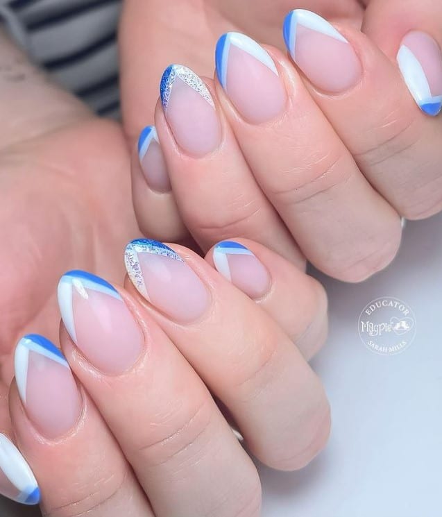 A closeup of a woman's hands with nude nail polish that has white-and-blue V-tips with silver glitter on select nails