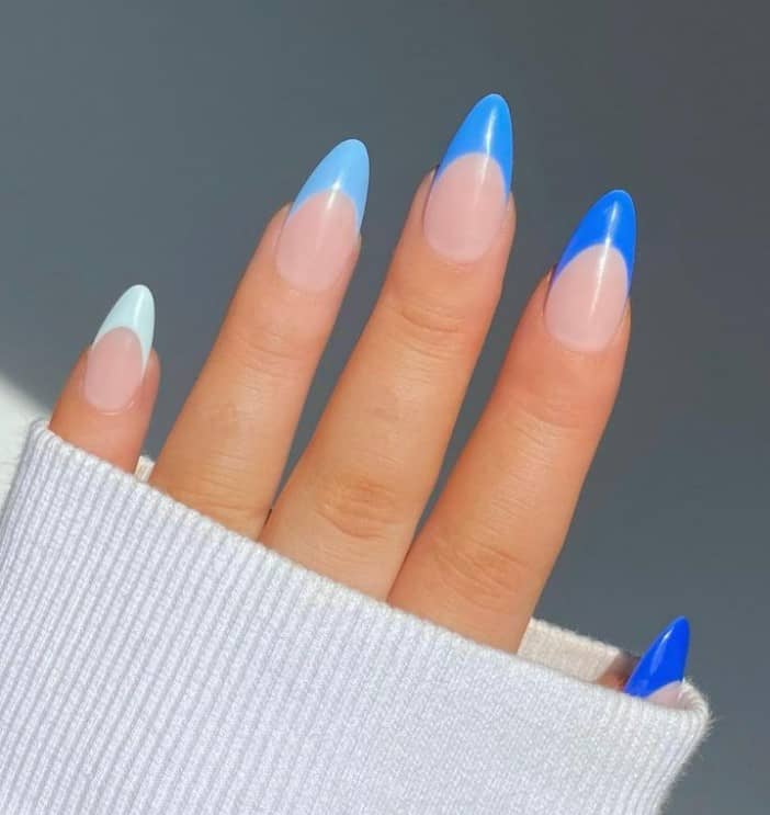 A closeup of a woman's hand with light nude nail polish that has long almond nails in different shades of blue