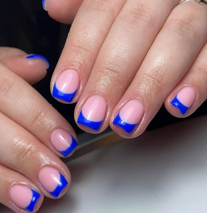 A closeup of a woman's hands with pink nail polish base that has thick electric blue French tips