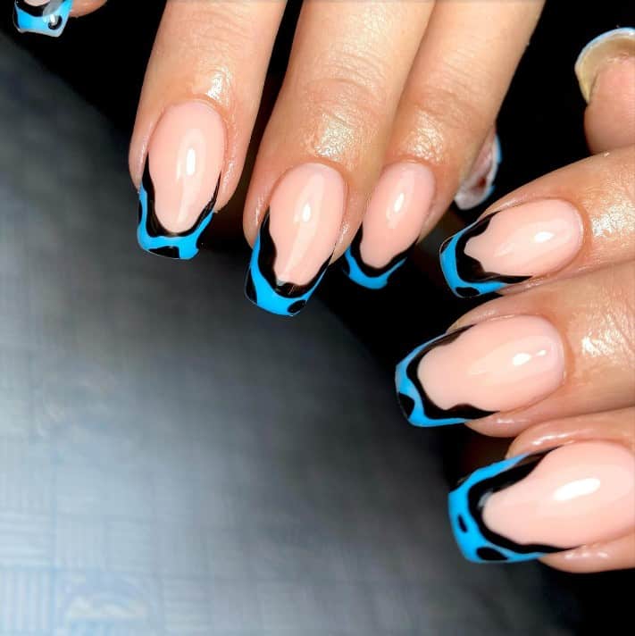 A closeup of a woman's hands with peach nail polish that has cow prints on neon blue French tips