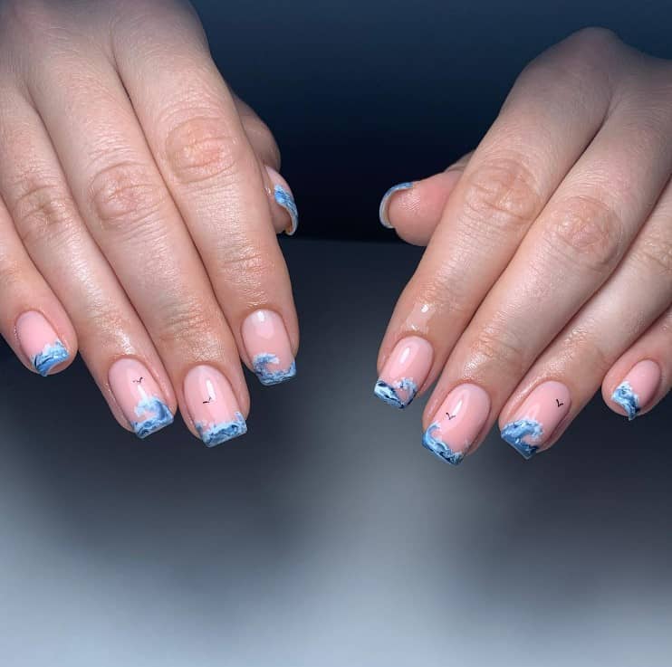 A closeup of a woman's hands with a glossy peach nail polish that has hand-painted ocean waves and flying birds nail art