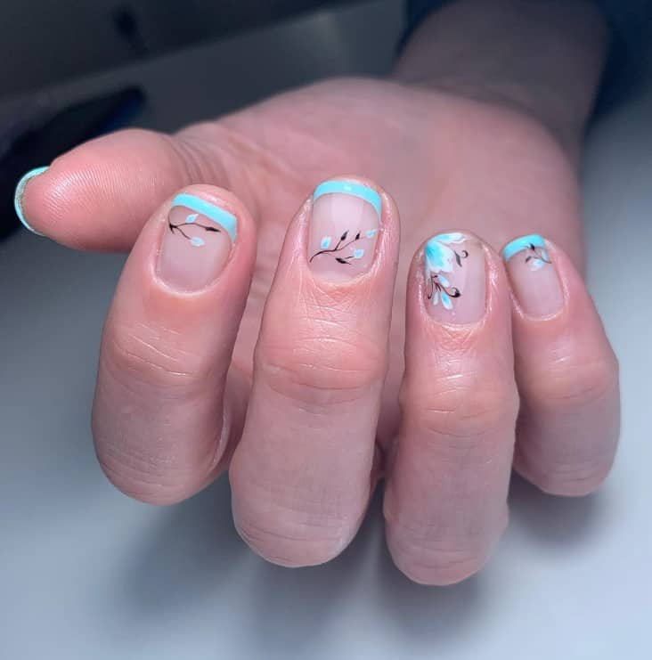 A closeup of a woman's hand with bare nails that has thinly lined aquamarine French tips with budding flowers and leaves nail art