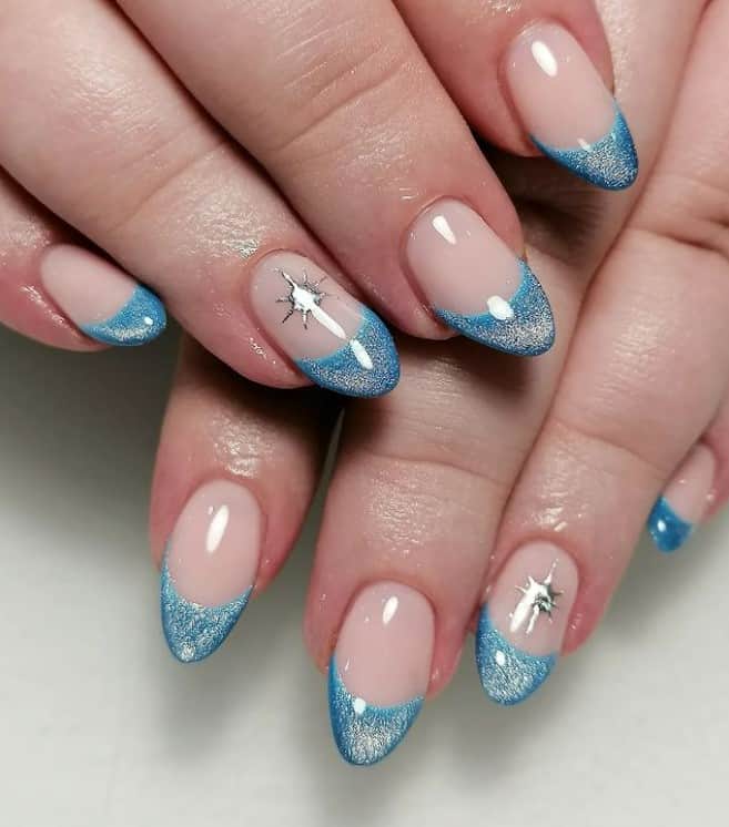 A woman's hands with a glossy nude nail polish base that has French tips in blue dip powder and a lone silver star on select nails