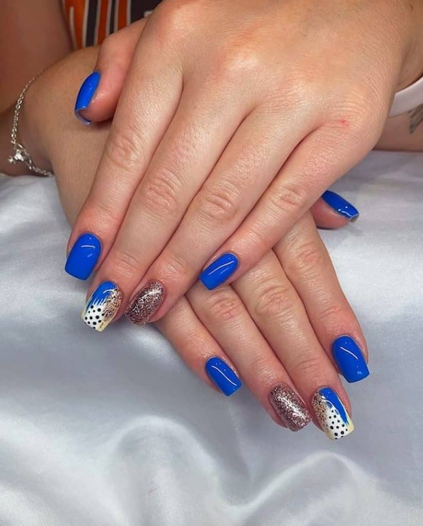 A woman's hand with glossy blue manicure with a playful blend of blue streaks, glitter splotches, and polka dots nail designs