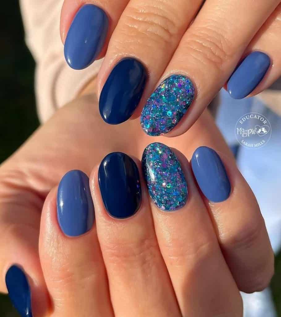 A closeup of a woman's hands with navy and denim blue nails that has glitter accent nails 
