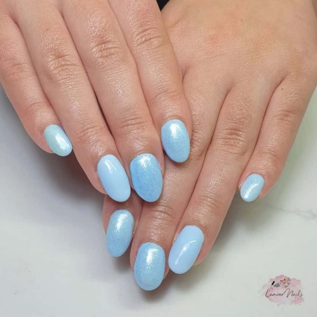 A closeup of a woman's hands with baby blue nails that has glitter  on select nails 