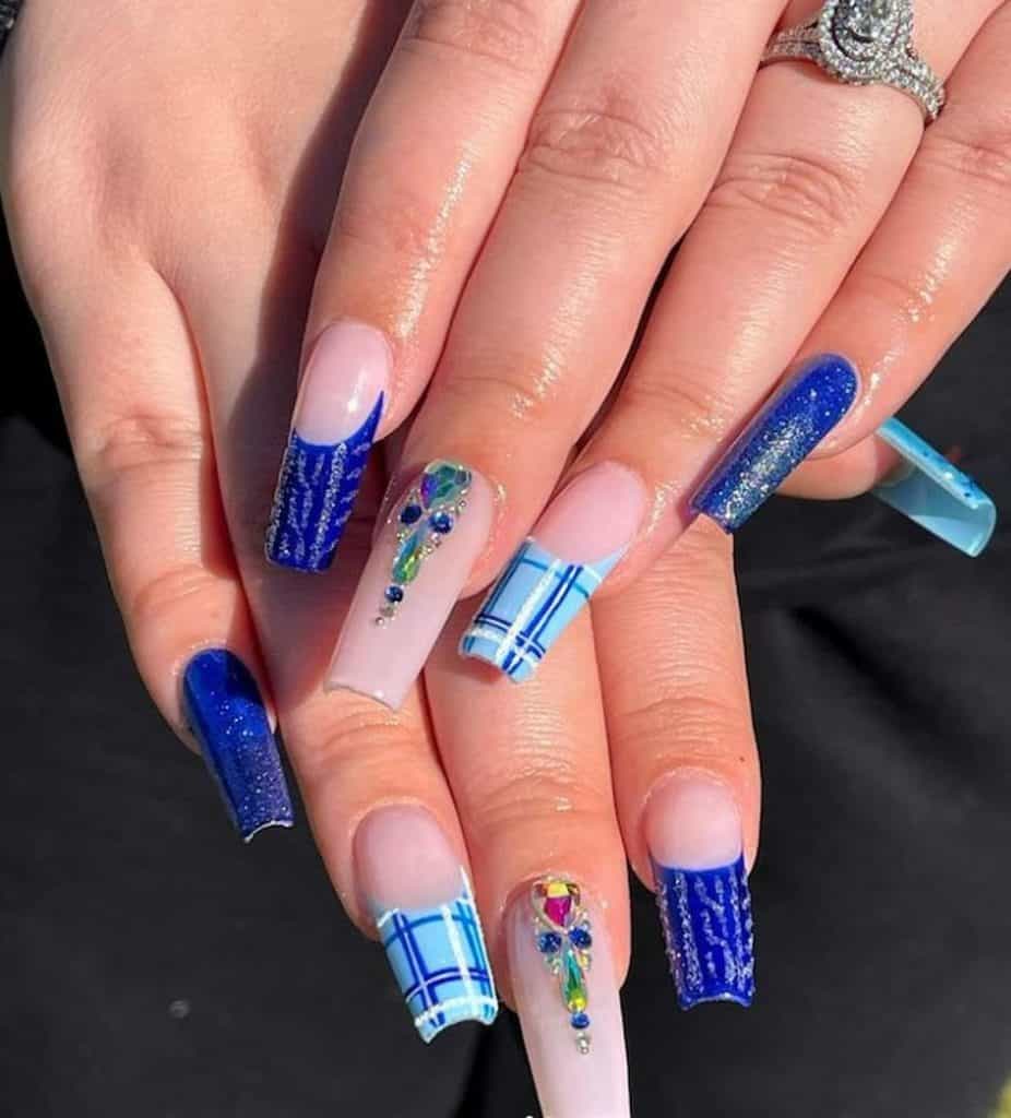 A closeup of a woman's hands with a blue nail polish that has colorful rhinestones, glitter and different patterns nail designs