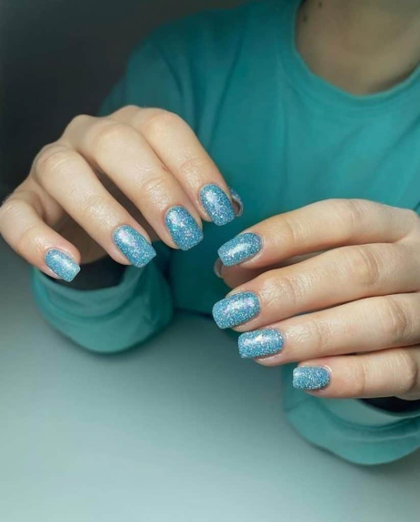 A woman's hands with blue nail polish that has silver glitter 