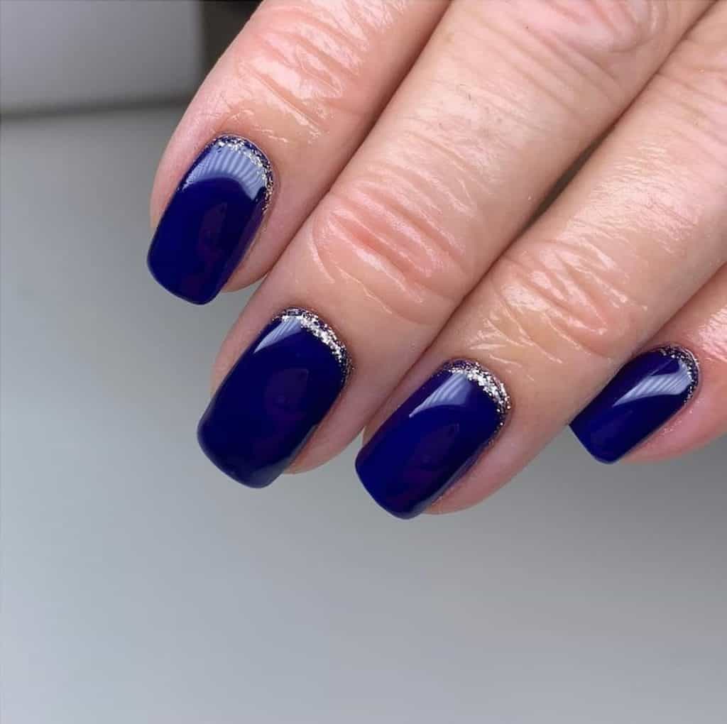 A closeup of a woman's hand with navy blue nail polish that has silver glitter