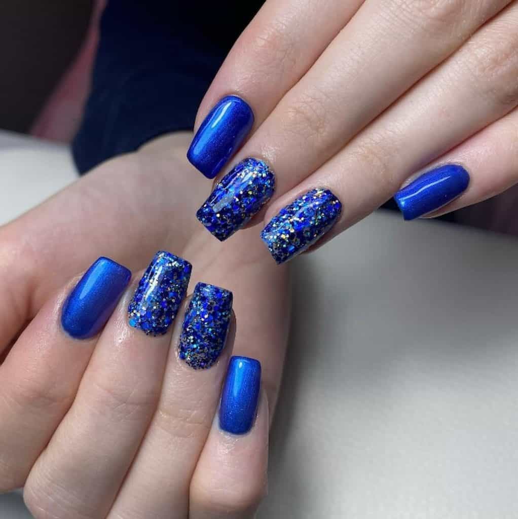 A closeup of a woman's hands with metallic royal blue nail polish that has large blue glitter flakes 