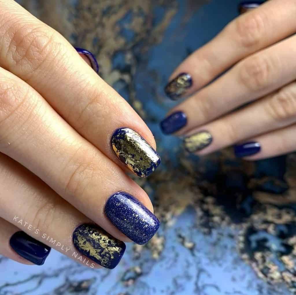 A closeup of a woman's hands with navy blue nail polish that has gold and silver glitter 