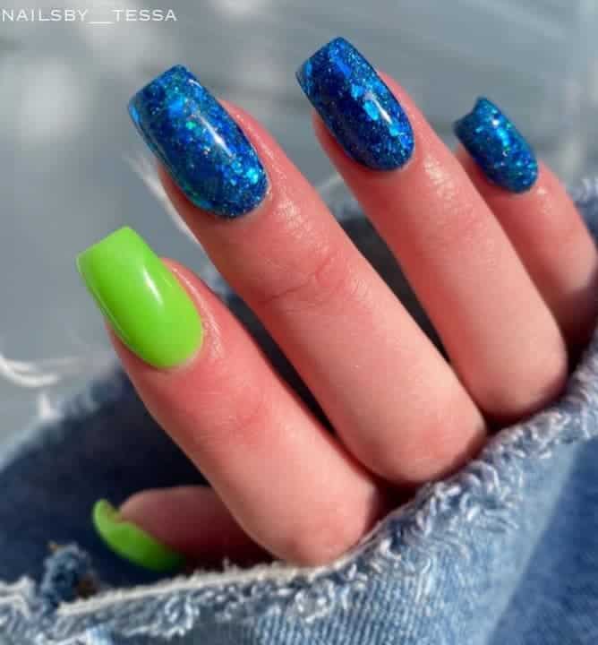 A closeup of a woman's hand with a combination of blue and green nail polish that has glitter 