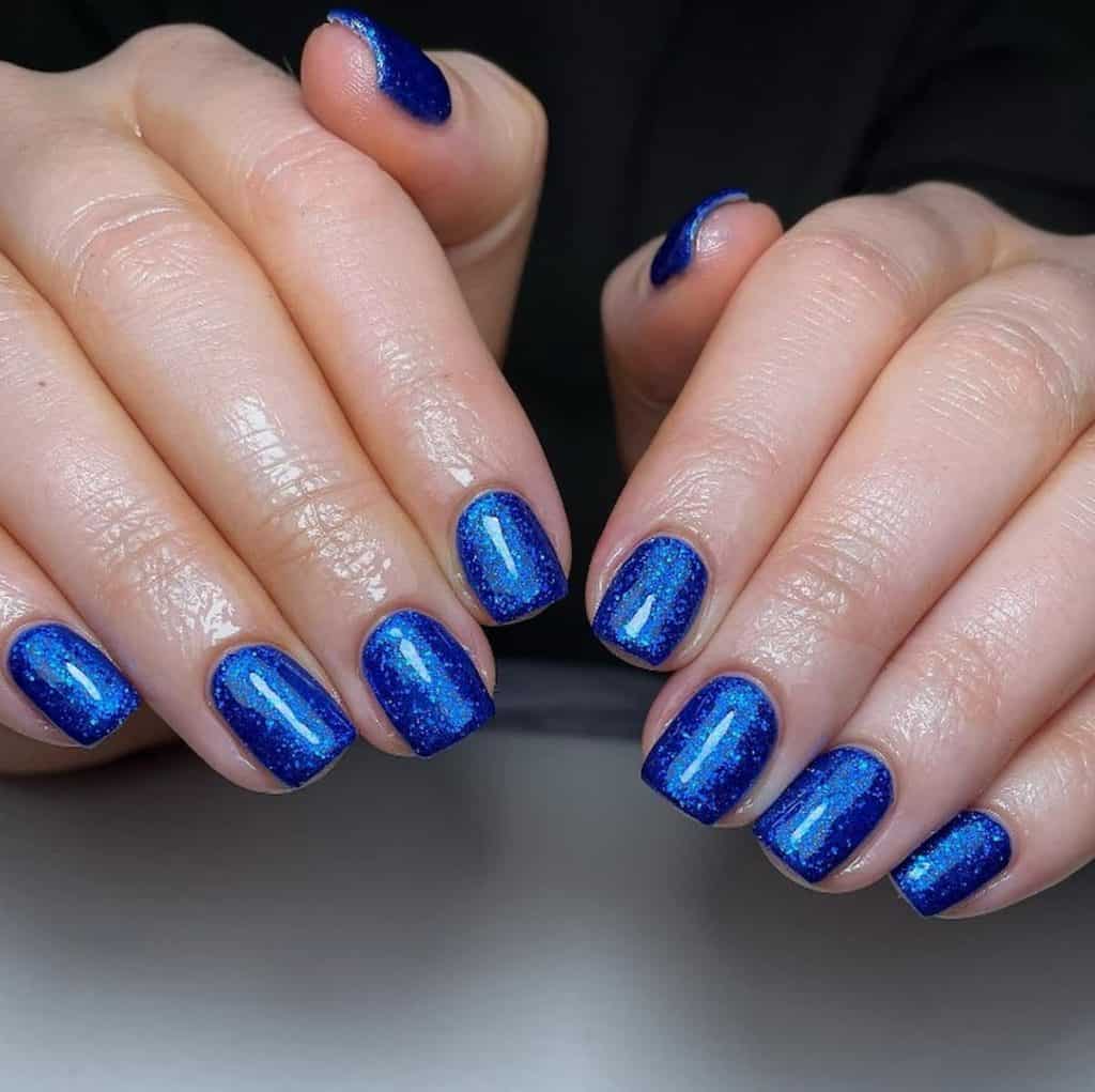 A closeup of a woman's hands with royal blue nail polish that has glitter