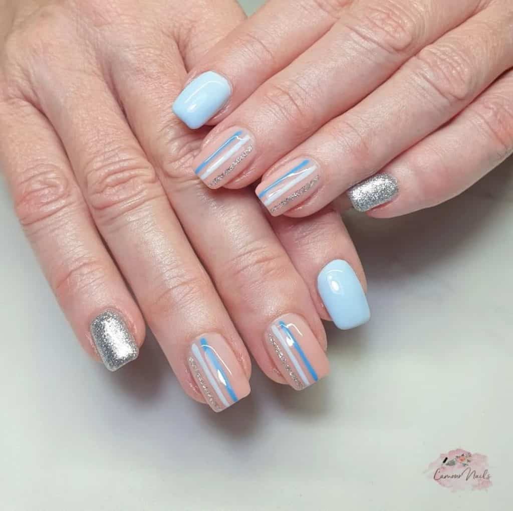 A woman's hands with a combination of light blue, nude and silver glitter nail polish that has multicolor stripes 