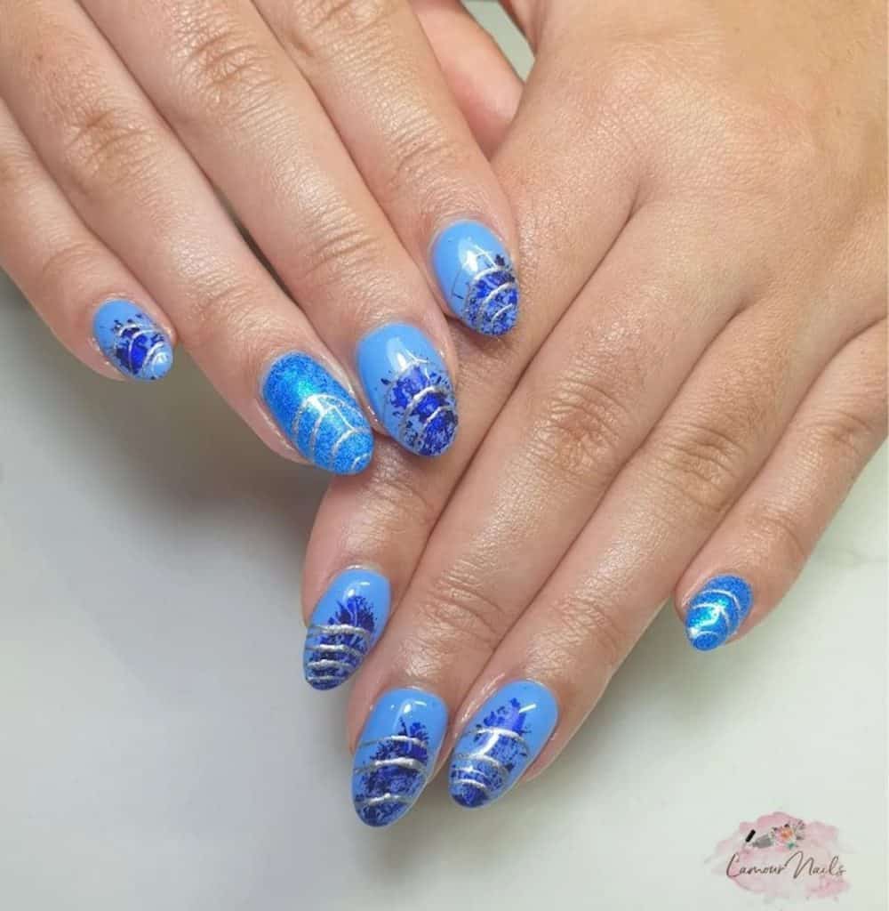 A woman's hands with blue nail polish that has glittery silver spirals nail designs