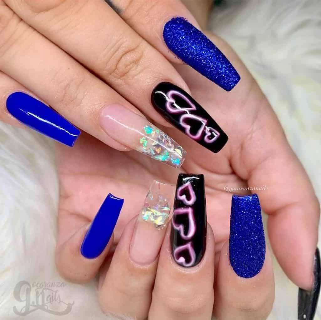 A closeup of a woman's hands with glossy blue, glittery blue nails, and black nails that has pink hearts, and clear nails with crystals at the tips