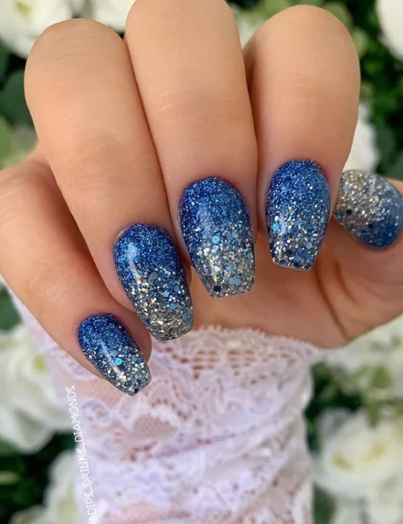 A closeup of a woman's hand with blue nail polish that has heavy chunks of silver glitter