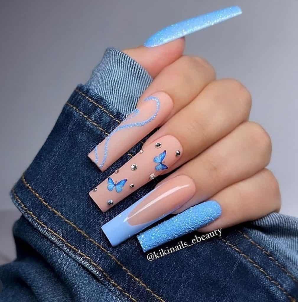 A closeup of a woman's hand with sky blue and nude manicure that has butterflies, swirly lines, and blue French tips 