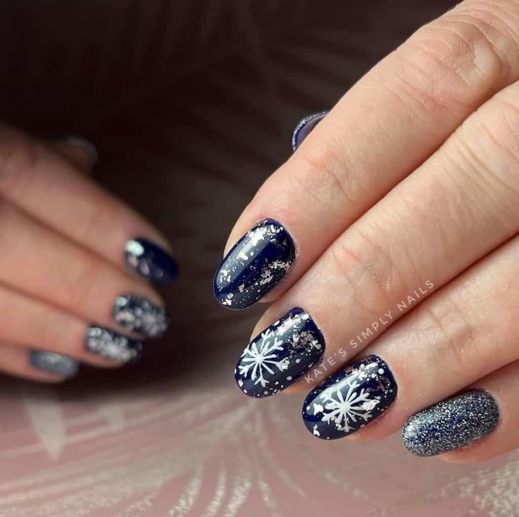 A closeup of a woman's hands with dark blue nails that has glitter and snowflakes nail designs