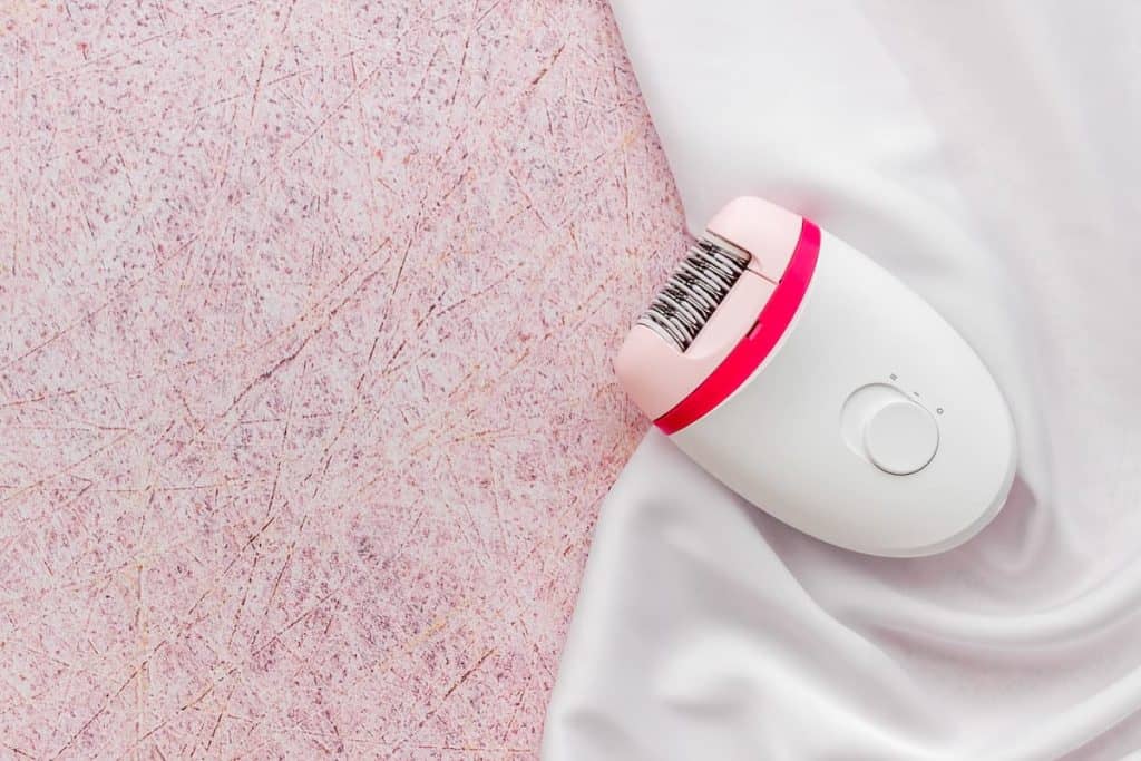 A pink and white epilator trimmer on a white fabric on top of a pink surface