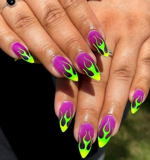 A closeup of a woman's hands with purple nail polish base that has a green nail polish flames art