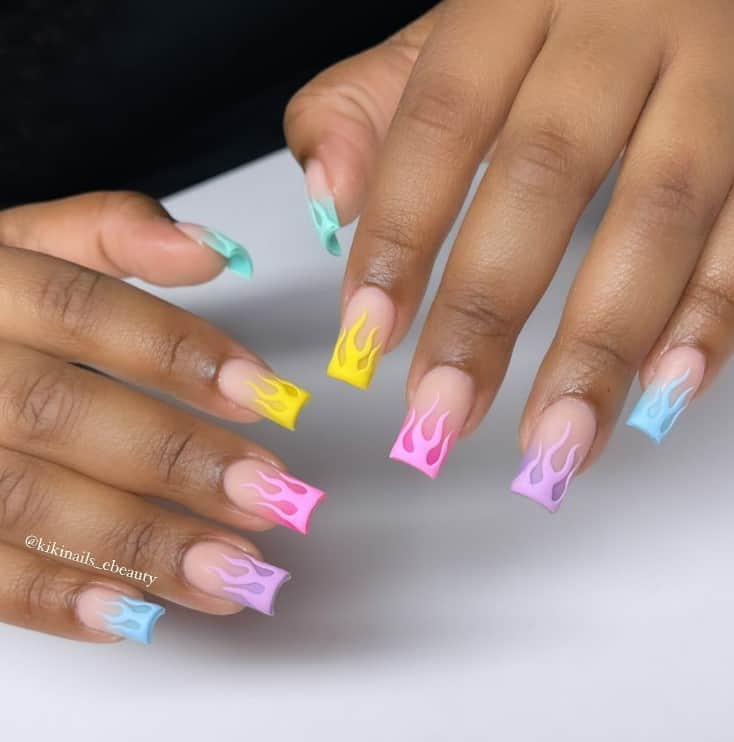 A closeup of a woman's hands with nude nail polish base that has multicolored pastel flames on nail  tips