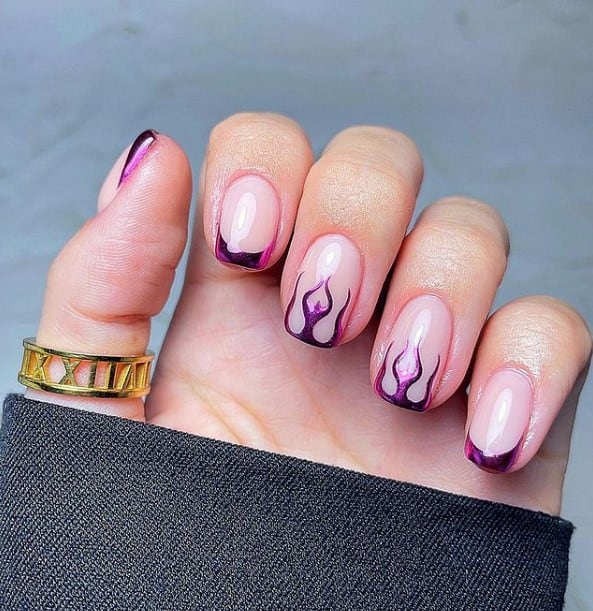 A closeup of a woman's hand with a glossy nude nail polish that has a chrome purple flames nail art