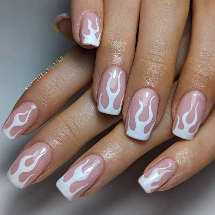 A closeup of a woman's hands with a glossy nude nail polish that has white flame nail design 