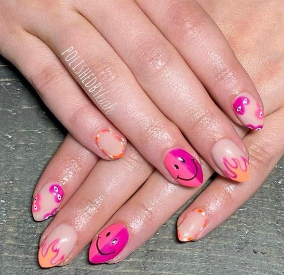 A closeup of a woman's hands with a nude nail polish that has pink outlined flames and cute smileys nail designs