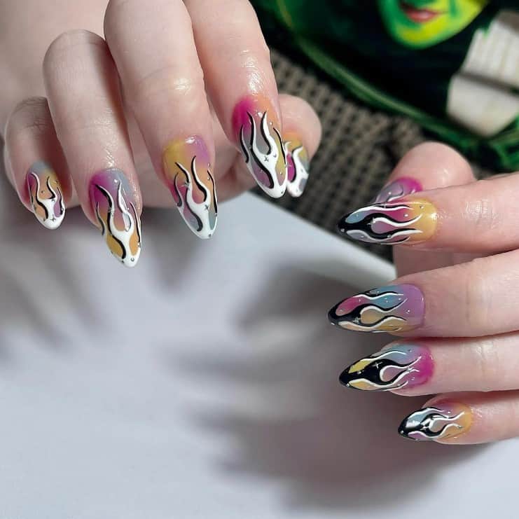 A closeup of a woman's hands with rainbow-themed nail polish that has black-and-white nail design flames