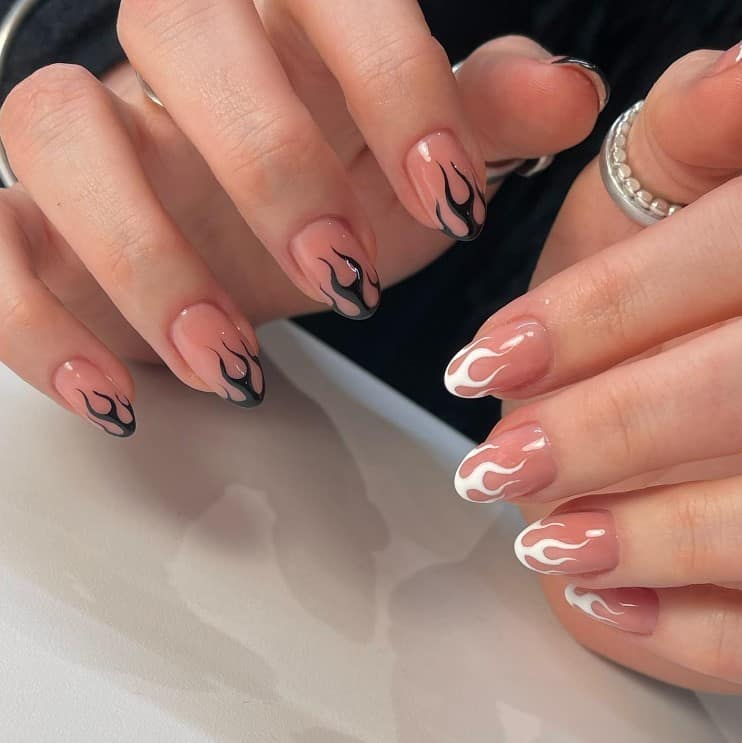 A closeup of a woman's hands with nude nail polish base that has black and white styled flames nail designs