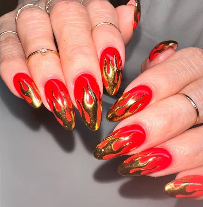 A closeup of a woman's hands with a bright red nail polish base that has blazing gold flames nail art