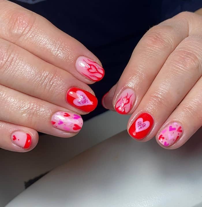A closeup of a woman's hands with pale pink nail polish that has cute pink heart and red fire nail designs